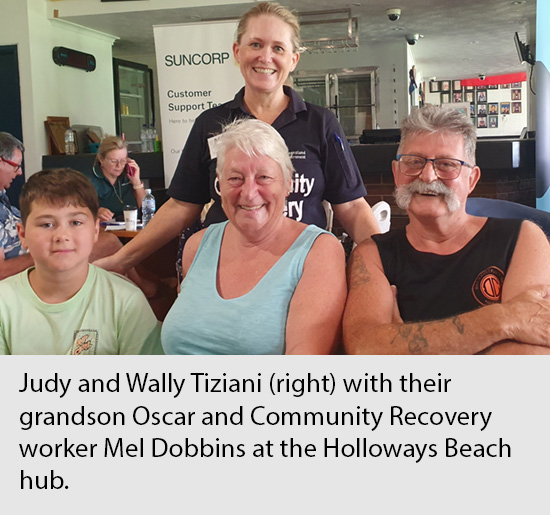 Family members affected by a disaster event sit, posing with smiles, with a standing Community Recovery worker at a Hub location in FNQ.